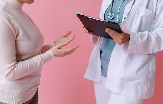 Profissional de saúde com prancheta conversa com paciente sobre adesão ao tratamento.