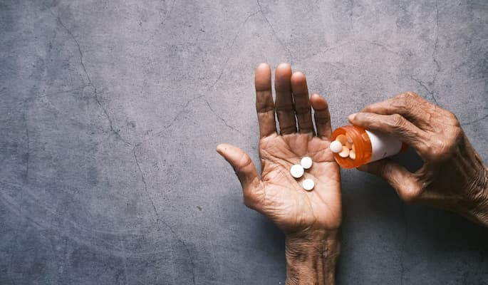 Mãos de uma pessoa idosa segurando comprimidos de dozemast enquanto despeja medicamentos de um frasco.
