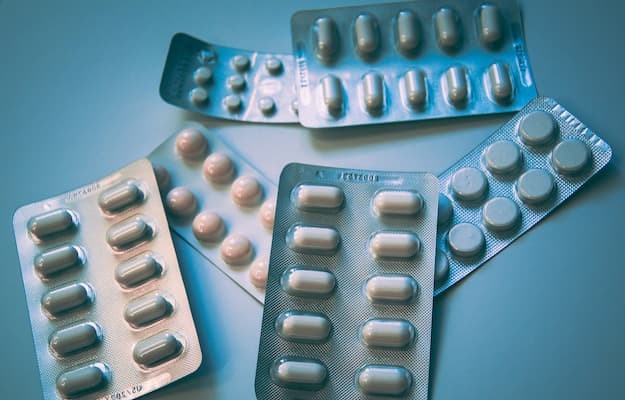 Cartelas de medicamentos controlados com comprimidos de e cápsulas sobre uma superfície azul.