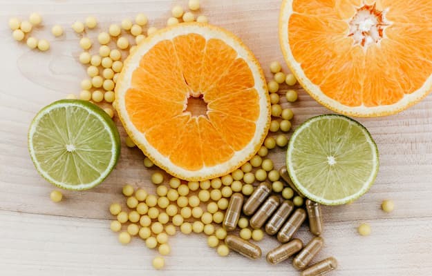 Fatias de laranja e limão ao lado de cápsulas e pequenas esferas de suplemento de vitamina B1.