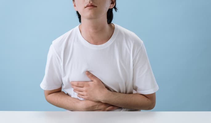 Homem com blusa branca em fundo azul com desconforto no estômagouso fazendo uso de esomeprazol.