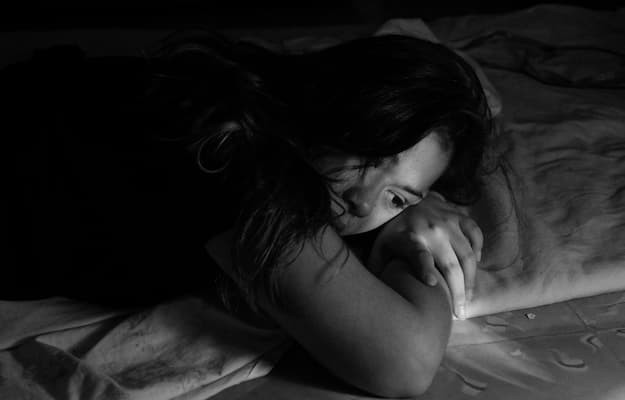 Mulher deitada na cama com expressão de tristeza e olhar distante com sofrimento emocional associado ao transtorno disfórico pré-menstrual (TDPM).