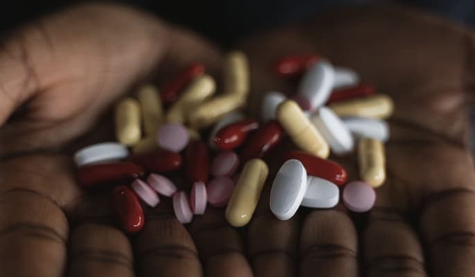 Pessoa que toma vários remédios segura diferentes comprimidos e cápsulas nas mãos.