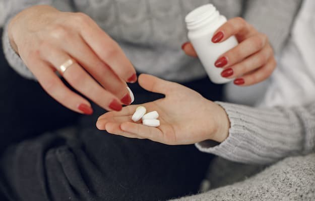 Pessoa colocando comprimidos de varfarina na palma da mão enquanto segura um frasco de medicamentos.