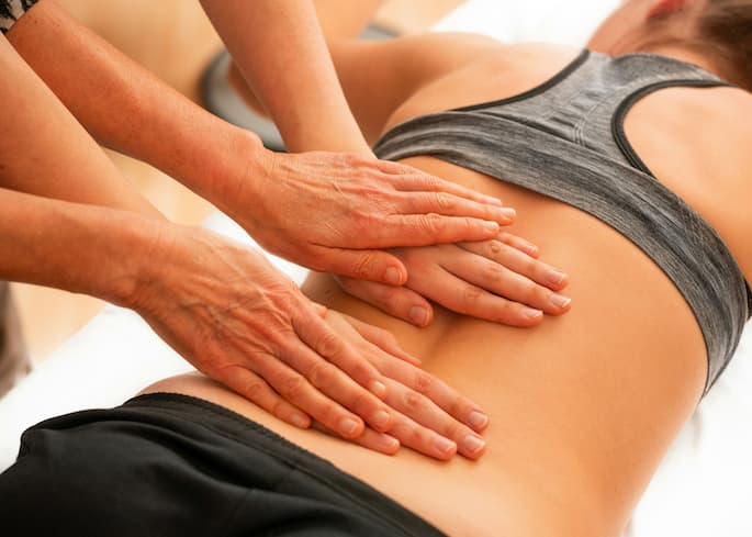 Pessoa deitada de bruços enquanto recebe uma massagem na região lombar com dor e inflamação tratada com celecoxibe.