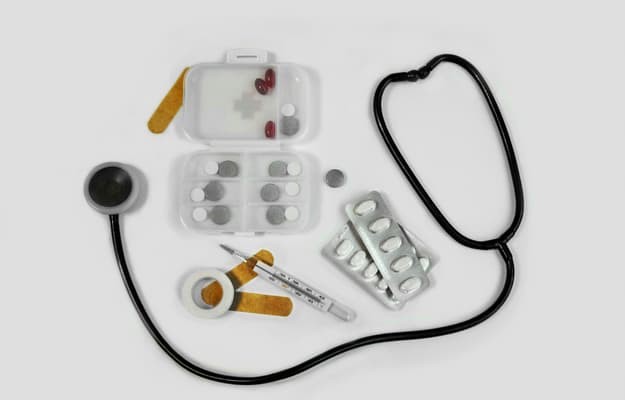 Kit de primeiros socorros com estetoscópio, termômetro, curativos, seringa e cartelas de remédio para pressão.