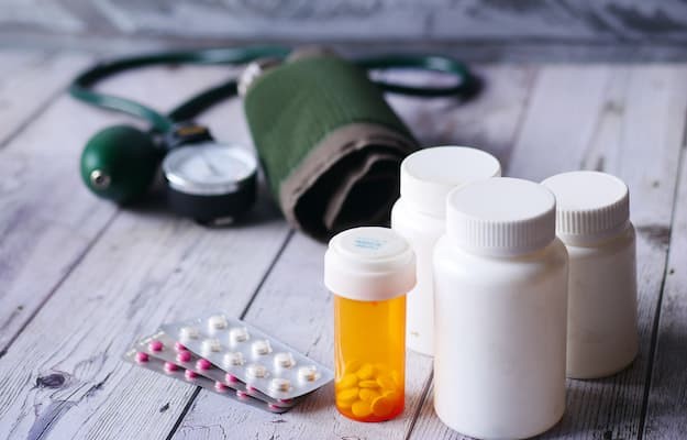 Frascos e cartelas de medicamentos ao lado de um aparelho de pressão com remédios de pressão.