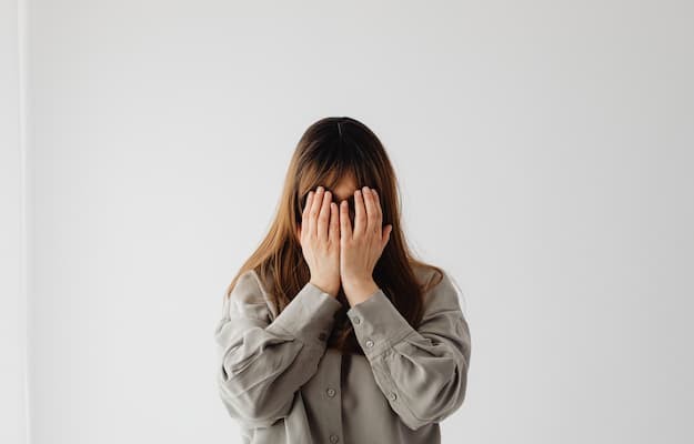 Mulher cobrindo o rosto com as mãos, representando ansiedade, medo e sintomas de fobia social.