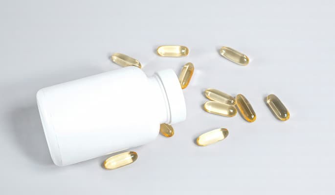 Frasco de vitamina B12 com cápsulas espalhadas sobre uma superfície branca.
