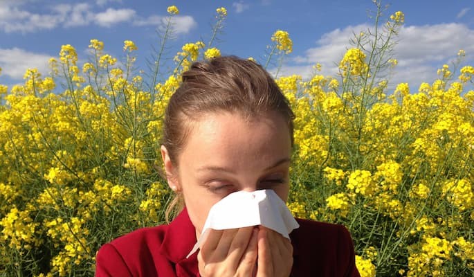 Mulher espirrando e cobrindo o nariz com um lenço em meio a uma crise de alergia tratado com dicloridrato de hidroxizina.