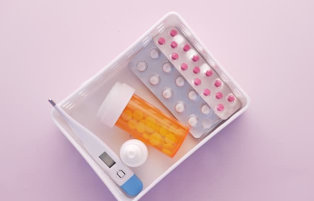 Estojo com medicamentos, termômetro digital e frascos organizados, representando a preparação de remédios para uma viagem.