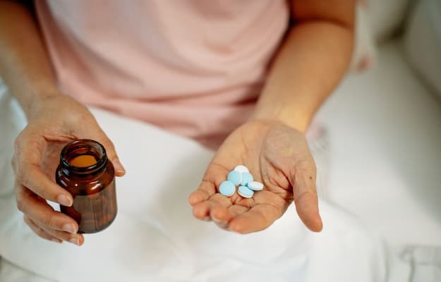 Pessoa segurando um frasco de medicamentos e vários comprimidos na palma da mão